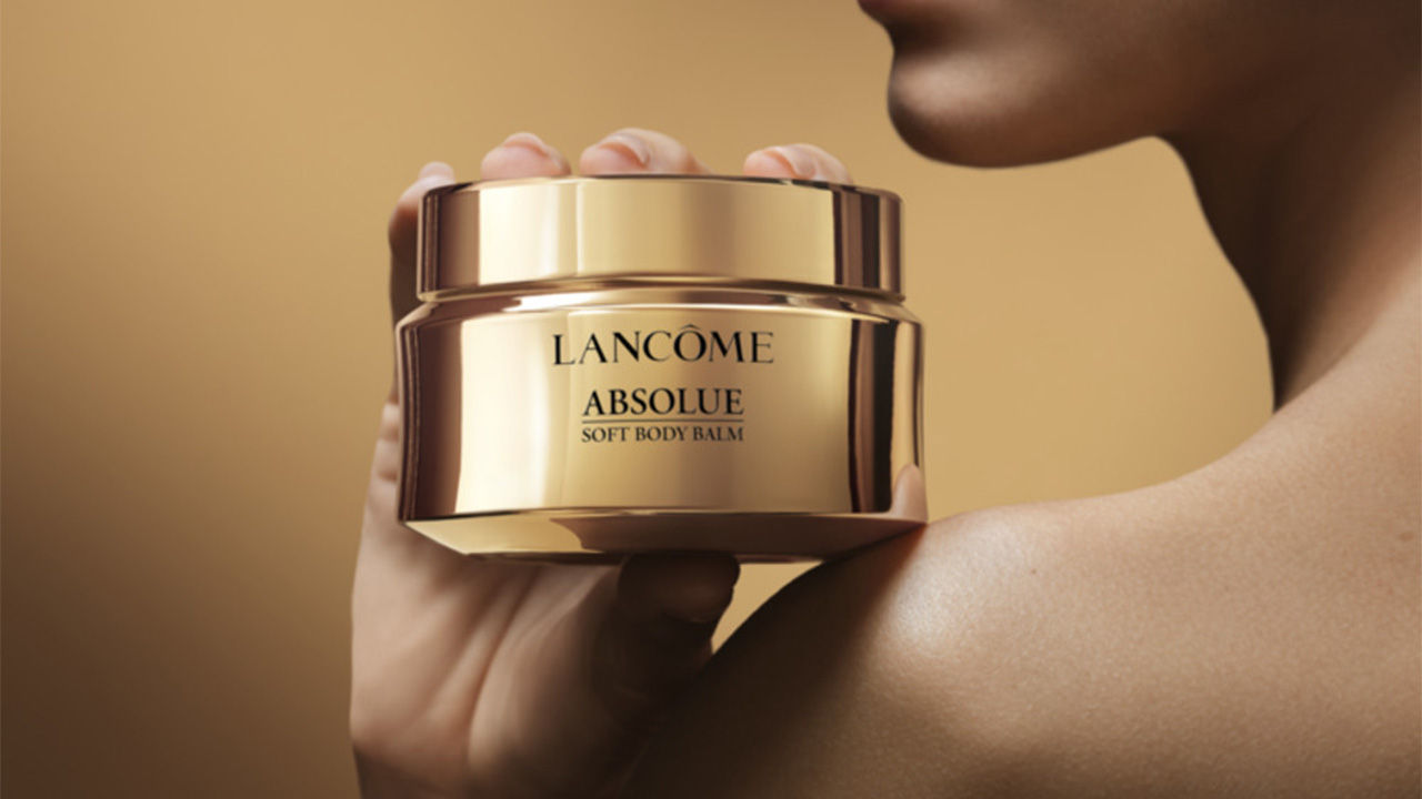 A woman holding a body balm in gold packaging from Lancome 