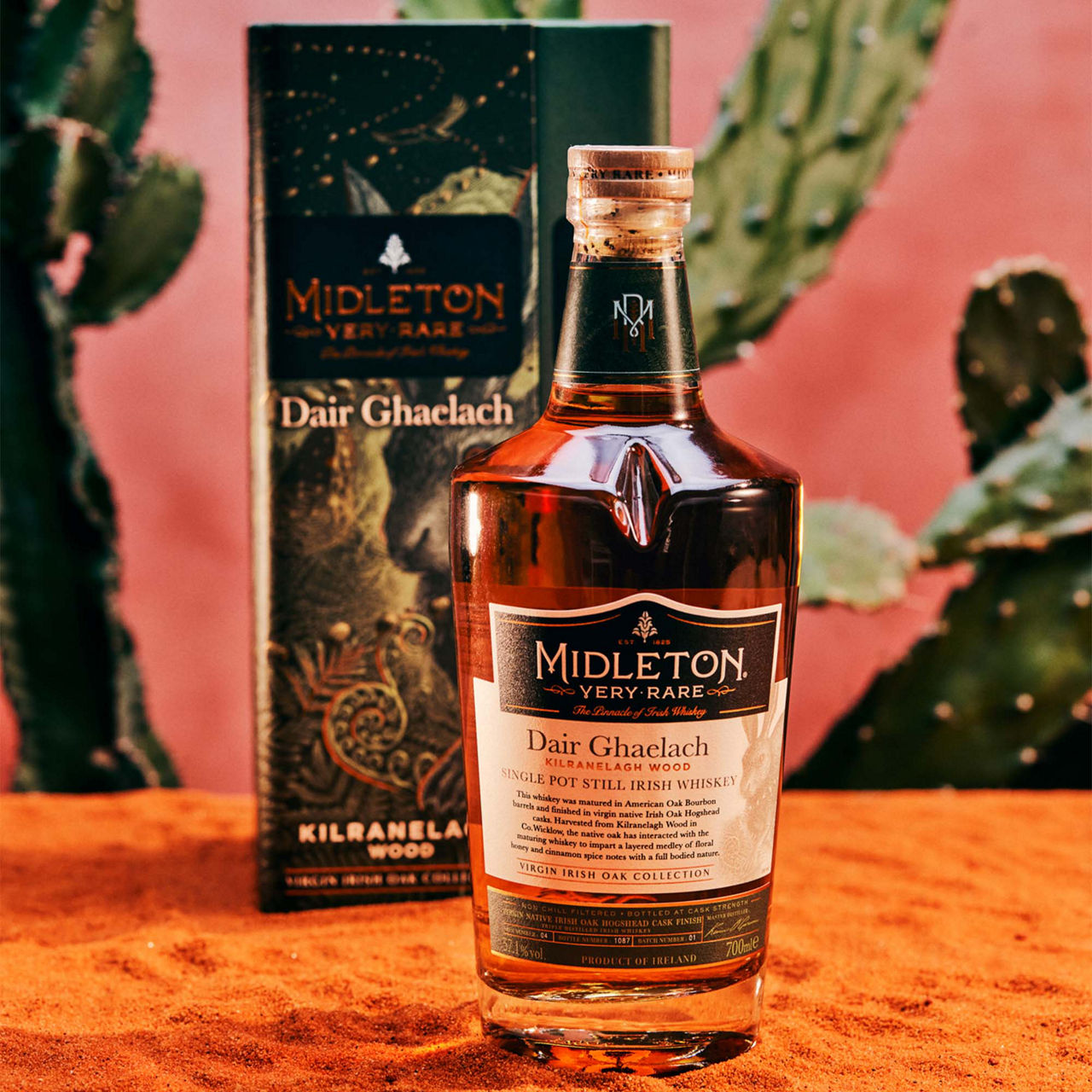 A bottle of Midleton Dair Ghaelach Irish whiskey with its box, set against a pink background and cactus plants.