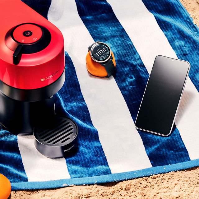 A phone, coffee machine and smart watch on the beach