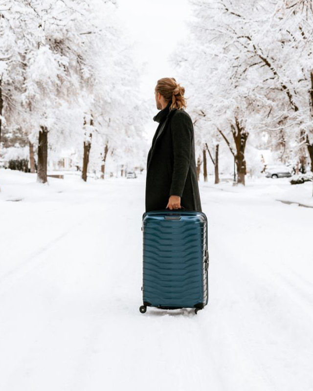 man walking in the snow with a blue suitcase