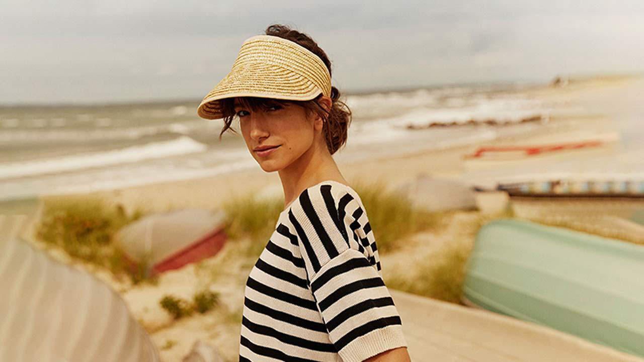 Model wearing hat in a sunny beach staring at the camera