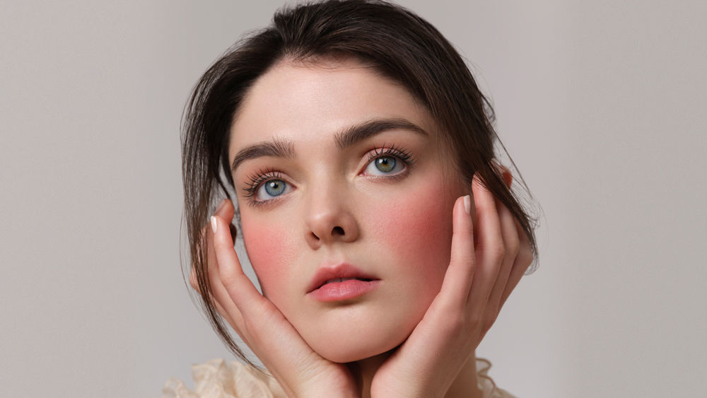 Model with rosy cheeks holding her face