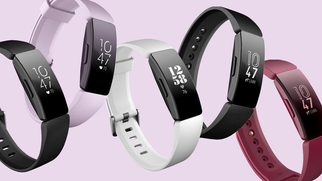 Five FitBit Watches on a lilac background in different colours. Black, Lilac, White, Black again and Red.